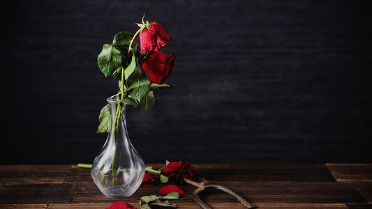 花瓣红色摄影照片_深灰色背景上枯萎的玫瑰和带落花瓣和落叶的木桌，悲伤情人节浪漫的设计理念，破碎，复制，空间。