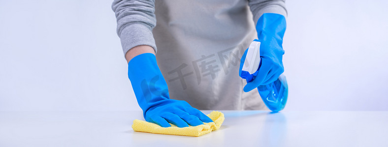 围裙的年轻女管家正在打扫卫生，用蓝色手套、湿黄抹布、喷瓶清洁剂、特写设计理念擦拭桌面。
