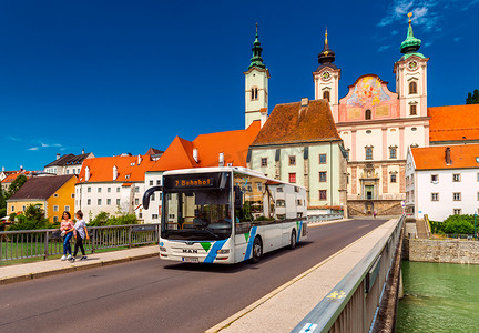 斯太尔 — 2020 年 6 月，奥地利：从斯太尔桥看现代巴士、步行女孩和圣迈克尔教堂