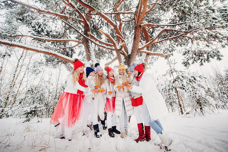 一大群带着橘子的女孩站在冬天的森林里。在白雪覆盖的森林里，穿着红白相间水果的女孩