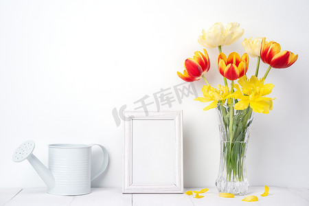家里墙壁摄影照片_玻璃花瓶中的郁金香花，相框放在白色木桌背景上，与家里干净的墙壁相映成趣，特写，母亲节装饰概念