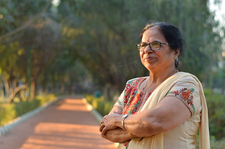 在印度新德里的夏天，穿着米白色萨尔瓦卡米兹旁遮普西装的公园里，聪明自信的北印度高级女性站立、思考和双手交叉/折叠