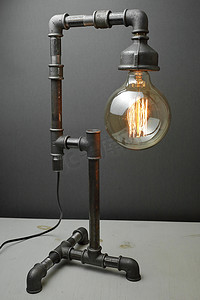复古灯由金属水管制成，灰色背景上有一盏爱迪生灯。