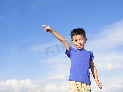 拳头指向摄影照片_快乐的小男孩指向蓝天背景的方向