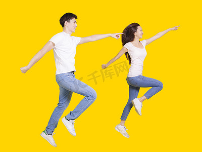 年轻夫妇在 copyspace 上跳跃和指指点点。隔离在黄色背景上。
