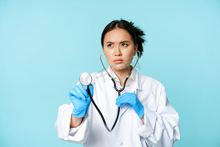 严肃医务工作者的形象，亚洲医生用听诊器听病人肺部检查，站在蓝色背景上