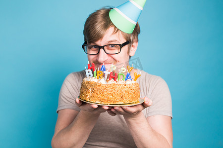 海报祝贺摄影照片_戴着问候纸帽的滑稽疯狂年轻人想咬掉一块祝贺蛋糕。