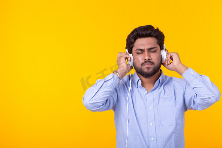印度男人在带复制空间的黄色背景中享受耳机中的音乐
