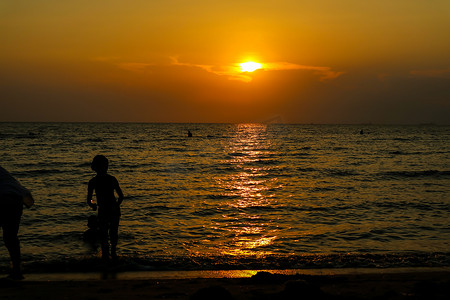剪影女人从孩子身边跑到海滩和日落