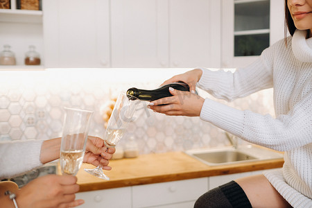 两个女孩在舒适的家庭环境中，在厨房里为圣诞节倒香槟。