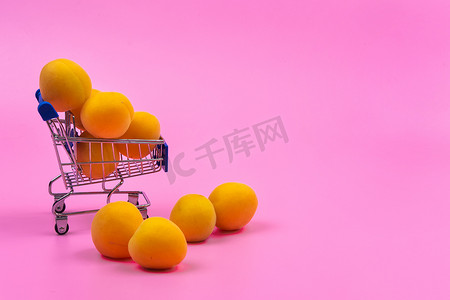 水果商店摄影照片_粉红色背景中装有杏子的购物篮。购物车