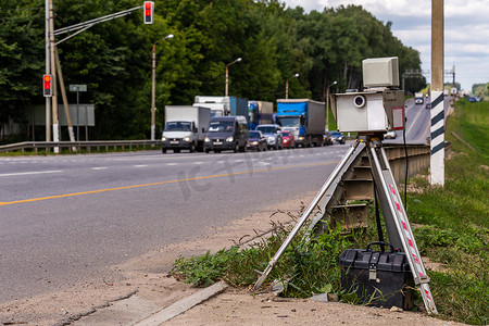 道路监控摄影照片_背景交通模糊的夏季白天道路上工作的三脚架移动测速摄像装置