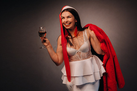 一位戴着圣诞帽和白色连衣裙的女人，手里拿着玻璃杯和红色毛皮大衣，黑色背景，圣诞节，假期