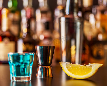 蓝色饮料摄影照片_流行的蓝色饮料在酒吧的背景上用瓶子射击 kamikaze，这是一种清爽的饮料