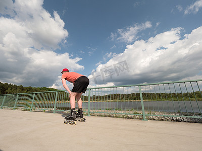 身穿红色 T 恤、带直排轮滑鞋的中年男子在夏季公园、流行的户外滑冰场上骑行。