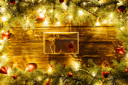 模糊的圣诞背景，在棕色木板上有杉树枝、仙女灯、礼盒和圣诞装饰