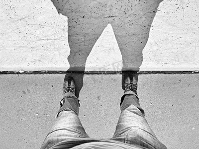 长腿摄影照片_男人长腿站在街道上，有阴影的混凝土墙