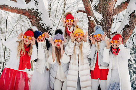 一大群带着橘子的女孩站在冬天的森林里。在白雪覆盖的森林里，穿着红白相间水果的女孩