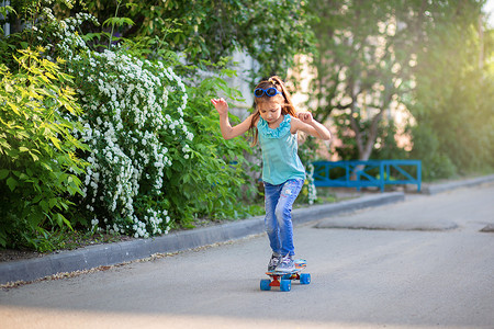 一个穿着牛仔裤和太阳镜的小女孩在院子里骑着滑板。