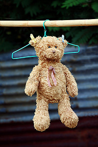 夹娃娃摄影照片_泰迪熊娃娃柔软地挂在晾干的晾衣绳上，在阳光下晒日光浴（选择性聚焦）
