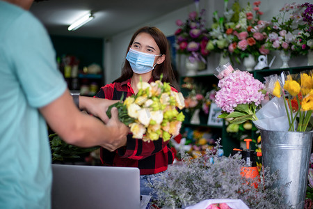 亚洲女性戴着面罩或防护面具抵御冠状病毒危机，一家小花店的花店老板拿着鲜花，在她的店里送给顾客
