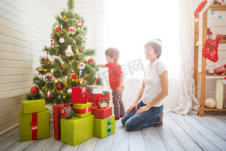 微笑的妈妈和她漂亮的小儿子在家里用小玩意装饰圣诞树