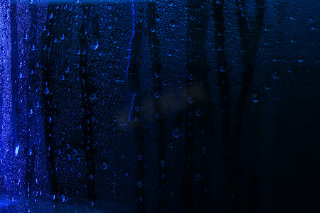 窗玻璃上的雨滴特写与蓝光。