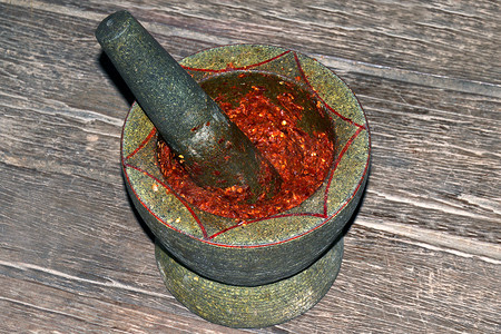 木背景砂浆石磨辣椒，砂浆和杵是红辣椒磨和咖喱配料大蒜，泰式红咖喱磨酱配料酸汤香料在砂浆中