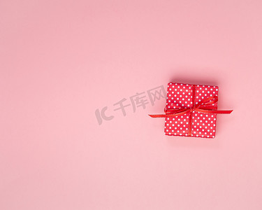 粉色背景活动摄影照片_红色礼品盒中的礼物，带蝴蝶结、粉色背景、顶视图、空白文本空间。