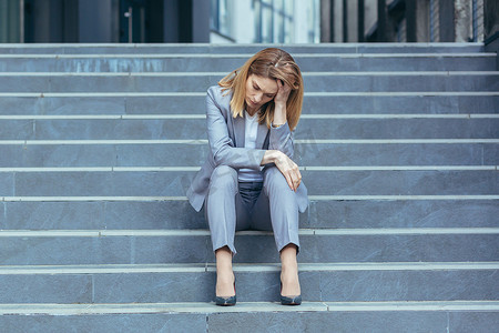 悲伤的女人摄影照片_坐在商务楼楼梯上的抑郁悲伤的女人，女商人