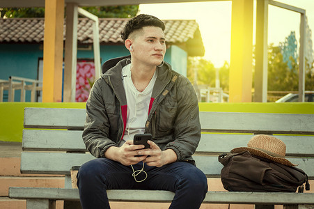 一个有魅力的男人在长凳上听音乐，拉丁男人坐在长凳上用手机听音乐
