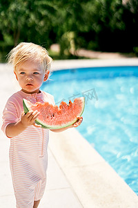泳池边有绿松石水的小女孩，拿着一块西瓜