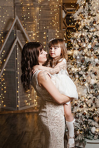 圣诞树旁，一个小女孩和她的母亲穿着浅色的节日服装。