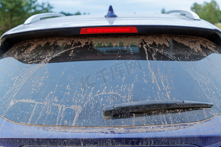 肮脏的汽车玻璃，有雨刷器和第三刹车灯，后窗覆盖着一层灰尘。
