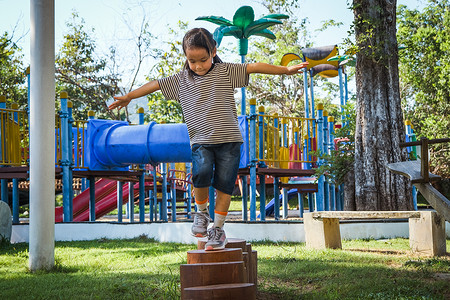 平衡木摄影照片_活跃的小女孩在公园的室外操场上走在平衡木上。