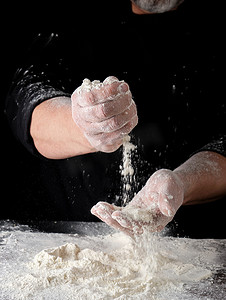 身穿黑色制服的厨师从手指中筛选白小麦面粉