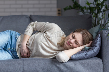 一个躺在沙发上生病的孤独女人的特写是腹痛，把手放在一边