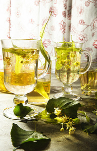 两杯新鲜制作的黄色菩提树茶，上面有菩提树的叶子和花朵。