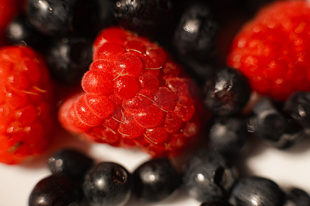 在明亮的阳光下，桌上的白色陶瓷盘子里放着许多多汁的鲜熟红草莓浆果