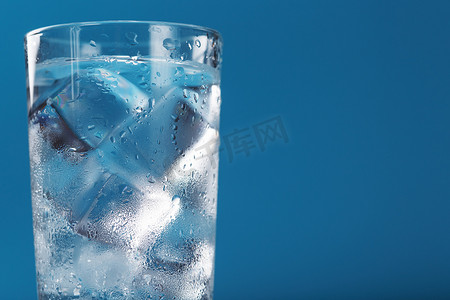蓝色背景上装有冰水和冰块的玻璃杯。