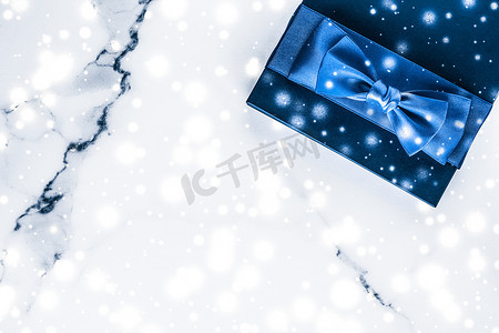 化妆品礼物摄影照片_冬季节日礼盒，配有蓝色丝绸蝴蝶结、大理石背景上的雪花，作为豪华美容品牌的圣诞和新年礼物，平铺设计