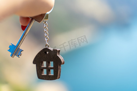 在大海的背景下，女性手中拿着房子形状的钥匙链钥匙。