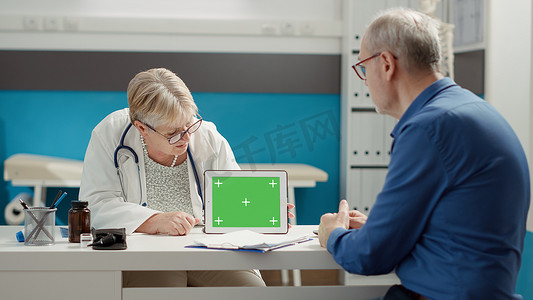 平板电脑绿幕摄影照片_高级医生指着带有水平绿屏的平板电脑