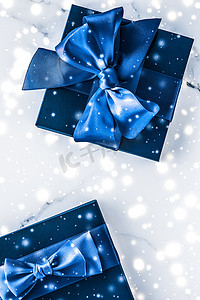 时尚礼盒摄影照片_冬季节日礼盒，配有蓝色丝绸蝴蝶结、大理石背景上的雪花，作为豪华美容品牌的圣诞和新年礼物，平铺设计