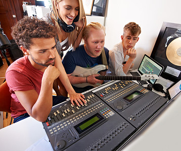 让我们听一下...四位年轻的音乐制作人坐在工作室的调音台前。