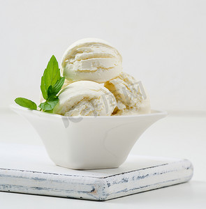 香草冰淇淋球摄影照片_白色陶瓷盘中带绿薄荷叶的香草冰淇淋球