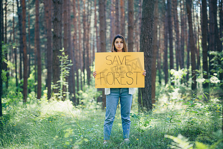 迎宾海报婚礼摄影照片_森林里年轻漂亮的女志愿者活动家，张贴着拯救森林的海报