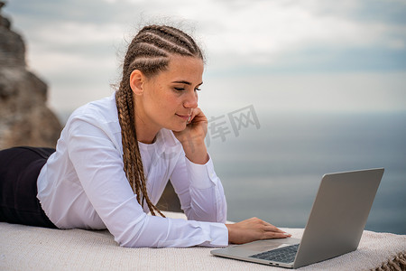 一位女士躺在露台上，在美丽海景的露台上用笔记本电脑键盘打字。