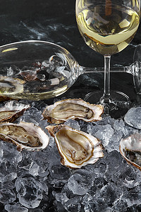 新鲜打开的牡蛎在冰和香槟中，在黑色的石头纹理背景上。