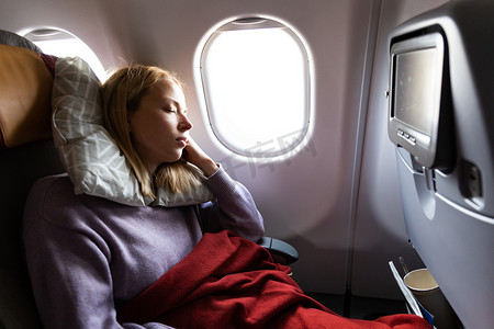 疲惫的金发休闲白种女士在乘飞机旅行时睡在座位上。